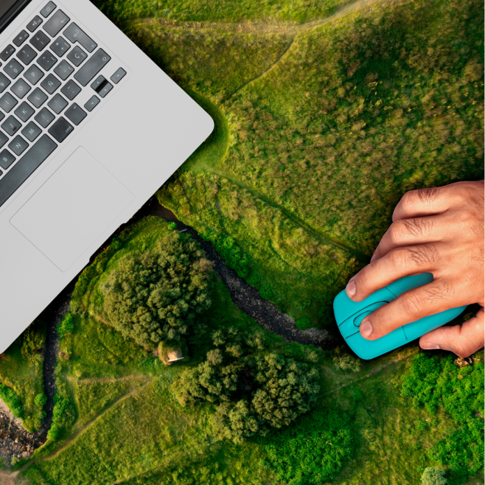 Designer working at a computer surrounded by plants, renewable energy icons, and low-carbon graphics representing sustainable digital design